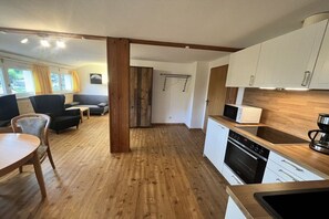 A modern kitchen with white cabinets, a wooden countertop, and a built-in oven. There is a dining area with a table and chairs, and a large window with curtains. - Holiday apartment in Todtnau with barbecue (Todtnau)
