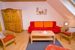A cozy living room with a red sofa, wooden cabinet, wicker chairs, and a coffee table. - Holiday apartment with 3 bedrooms (Colmberg)