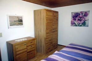 A bedroom with a wooden wardrobe, a bed with a purple-striped bedspread, and two paintings on the walls. - Holiday apartment with 3 bedrooms (Colmberg)