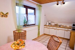 A small kitchen with white cabinets, a sink, and a microwave. There is a window with a curtain, a potted plant, and a table with a basket and a floral arrangement. - Holiday apartment with 3 bedrooms (Colmberg)