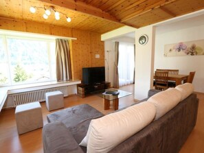 A cozy living room with a sofa, a coffee table, and a television. There is a window with curtains, a radiator, and a clock on the wall. - Bündalodge 1028 Appartement/Fewo, Dusche oder Bad, WC 4-Zimmerwohnung by Interhome (Davos)