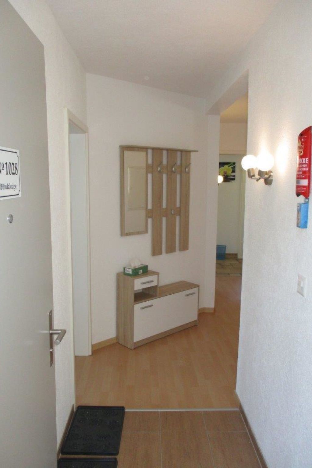 Un pasillo con un armario de madera, una mesita con una caja de pañuelos y un cartel que indica el número de habitación 1028.