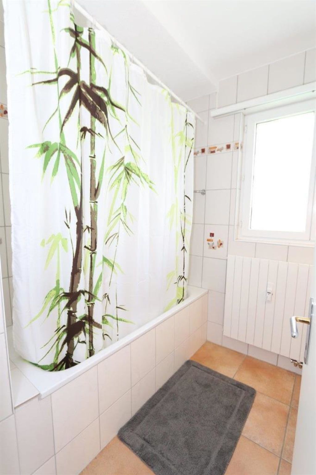 Een badkamer met een douchegordijn van bamboe, een raam en een handdoek op de vloer.