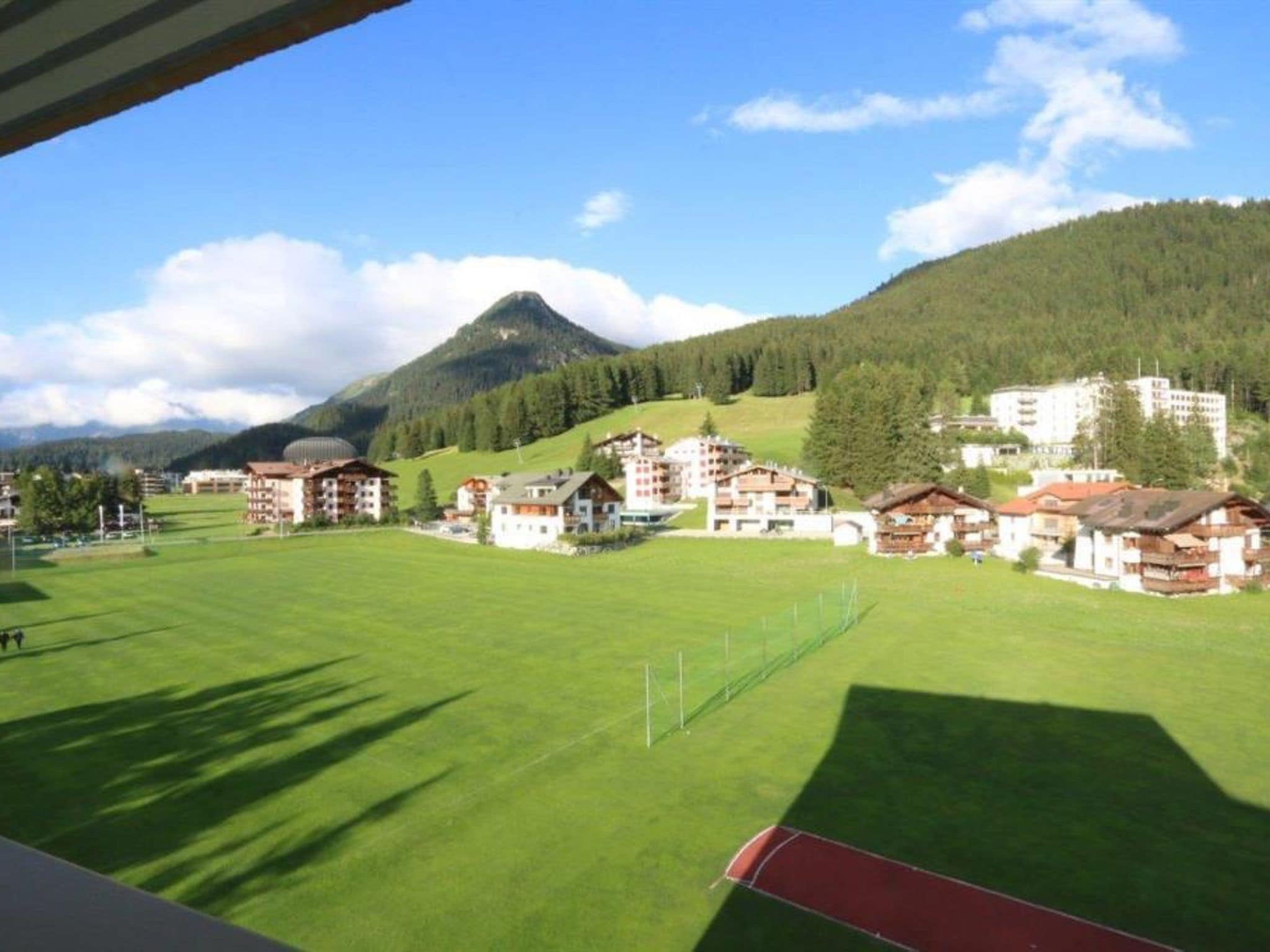 Vista di un complesso alberghiero con diversi edifici, un prato verde e una montagna sullo sfondo.