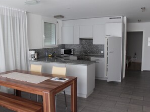 A modern kitchen with a central island, white cabinetry, and a dining area with a wooden table. - Mühlestrasse 3B (MAI) Appartement/Fewo, Dusche oder Bad, WC 3½-Zimmerwohnung by Interhome (Davos)