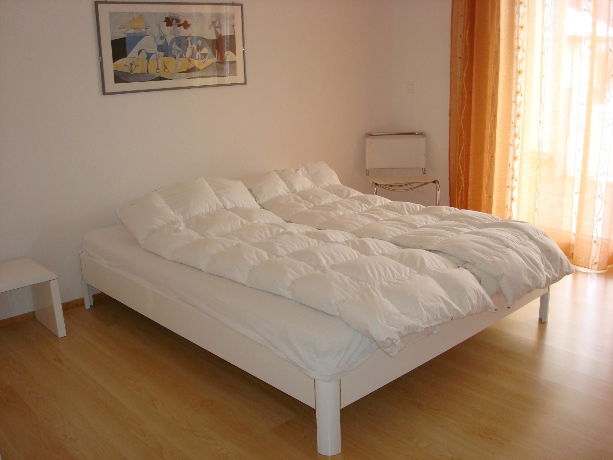 Een netjes opgemaakt bed met witte beddengoed in een kamer met houten vloeren en een schilderij aan de muur.