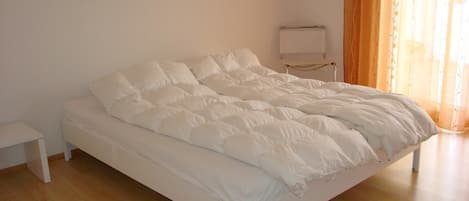 Een netjes opgemaakt bed met witte beddengoed in een kamer met houten vloeren en een schilderij aan de muur.