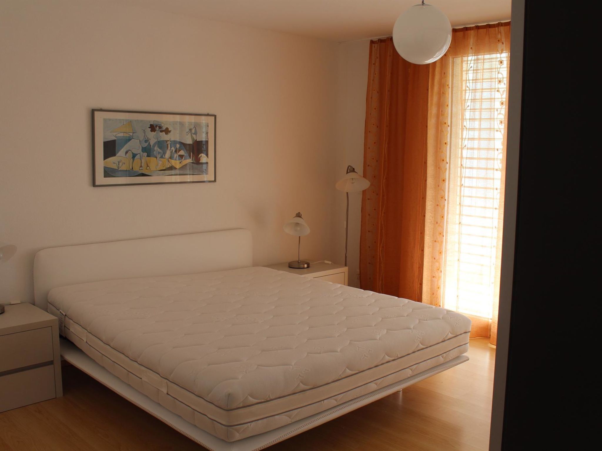 Quarto com cama, mesa de cabeceira, luminária e um quadro na parede.