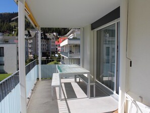 A balcony with a table and chairs, a glass door, and a view of neighboring buildings. - Mühlestrasse 3B (MAI) Appartement/Fewo, Dusche oder Bad, WC 3½-Zimmerwohnung by Interhome (Davos)