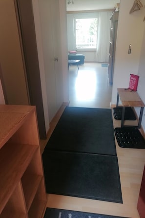 A room with a wooden wardrobe, a black mat on the floor, a small table with a red bag, and a view of a balcony with a sofa. - Talstrasse 22 App 12 Appartement/Fewo, Dusche oder Bad, WC 2-Zimmerwohnung by Interhome (Davos)
