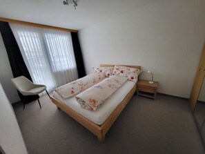 A bedroom with a bed, a chair, a bedside table, and a window with curtains. - Talstrasse 22 App 12 Appartement/Fewo, Dusche oder Bad, WC 2-Zimmerwohnung by Interhome (Davos)