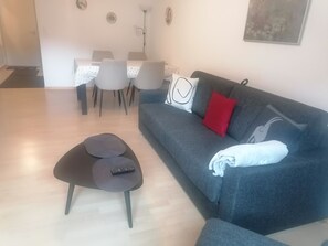 A modern living room with a grey sofa, a small black ottoman, and a dining area with a white tablecloth. - Talstrasse 22 App 12 Appartement/Fewo, Dusche oder Bad, WC 2-Zimmerwohnung by Interhome (Davos)