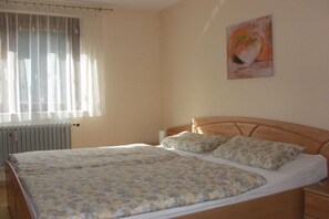 A bedroom with a bed, a radiator, a window with curtains, and a painting on the wall. - Holiday apartment with 2 bedrooms (Oberried)