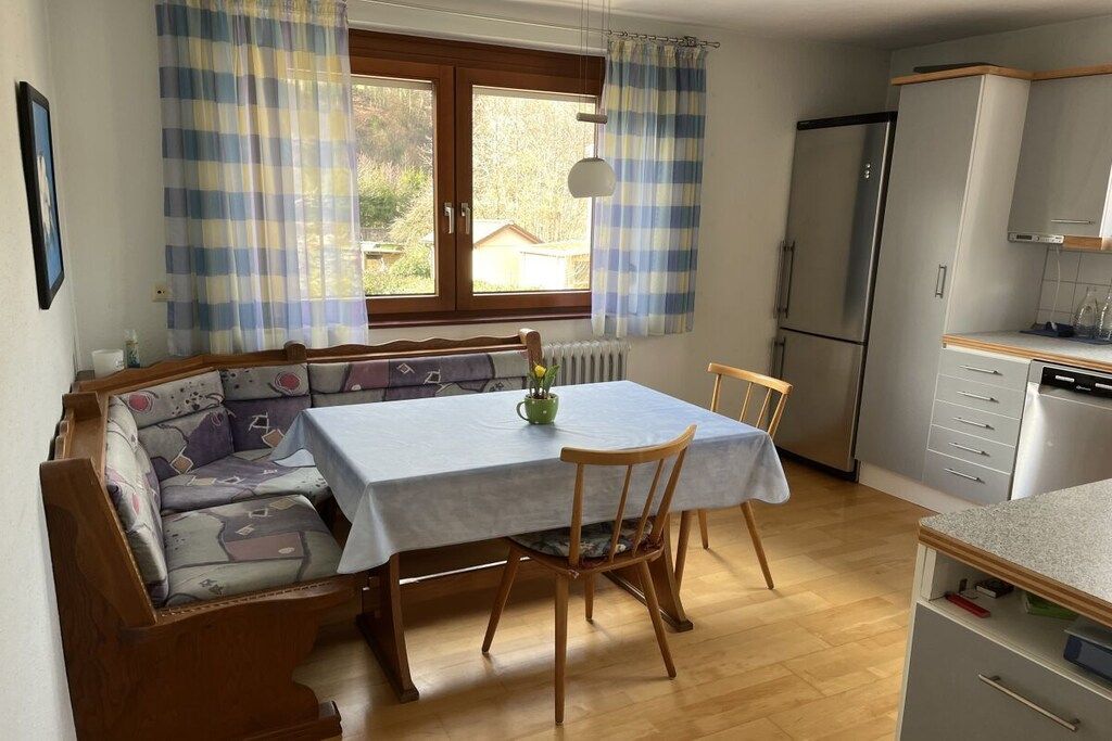 A cozy dining area with a table and chairs, a sofa, a radiator, a window with curtains, and a kitchen area with cabinets and appliances.