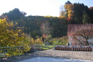 A fenced garden area with a gravel path, trees with autumn foliage, and a building with a red roof. - Holiday apartment with 2 bedrooms (Oberried)