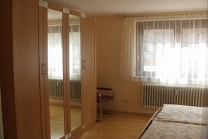 Een slaapkamer met een bed, een kast, een radiator en een raam met gordijnen.