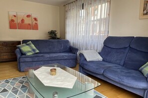 A living room with two blue sofas, a glass coffee table, and a geometric patterned rug. - Holiday apartment with 2 bedrooms (Oberried)