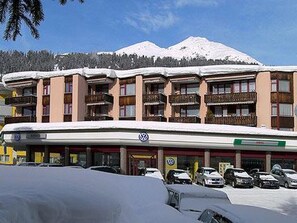 Ein mehrstöckiges Hotel mit Balkonen, einem Parkplatz und verschneiten Bergen im Hintergrund.