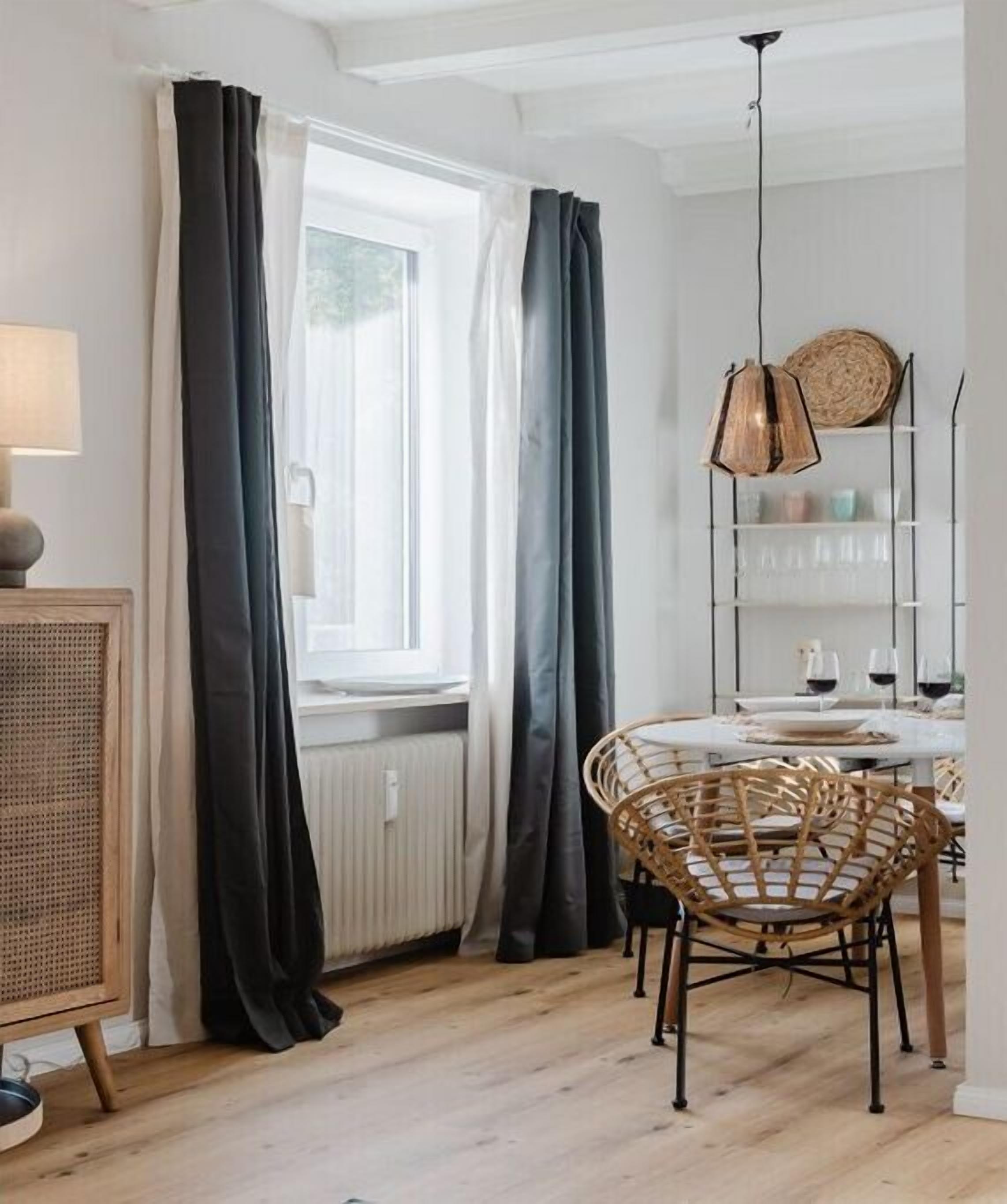 A dining area with a round table, wicker chairs, a hanging light fixture, and a window with curtains.