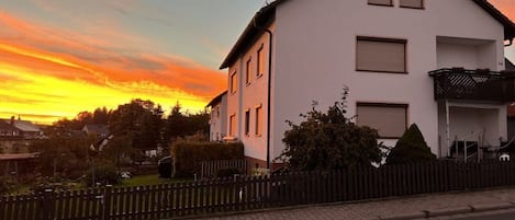 Un edificio residencial de dos pisos con fachada blanca, un balcón y una cerca negra al frente.