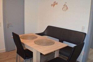 Een intieme eethoek met een houten tafel en zwarte stoelen, een muur met een bord met koffie-gerelateerde tekst, en een deur op de achtergrond.