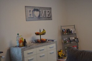 A room with a wall-mounted sign that reads 'HOME,' a small table with a fruit basket, a shelf with books, and a toy car on the floor. - Holiday apartment with 1 bedroom (Selb-Plößberg)