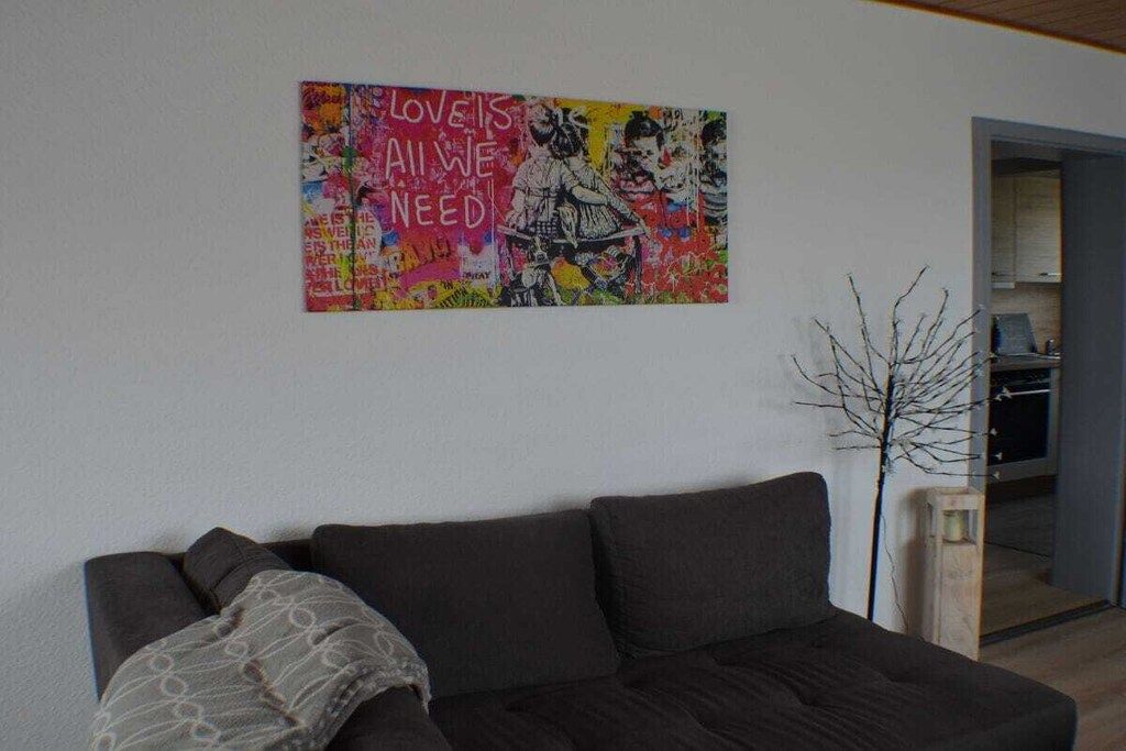 Ett vardagsrum med en soffa i mörk färg, ett dekorativt väggobjekt och en växt.