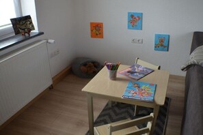 Een kinderkamer met een klein tafeltje, een krukkonen en wanddecoraties.