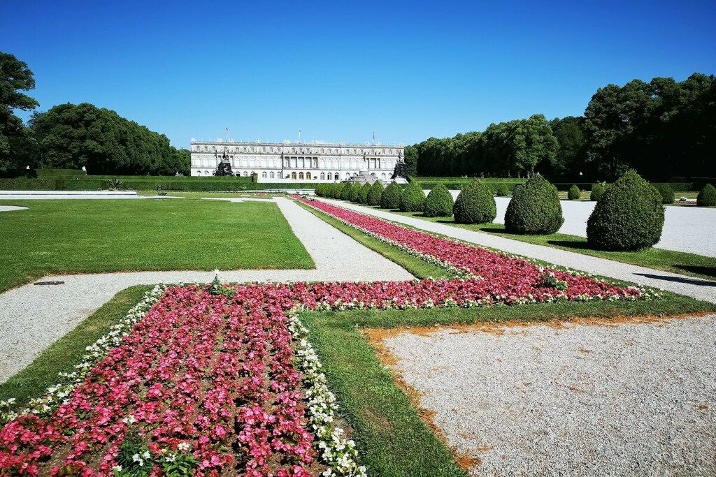 Un jardin à la française, avec des parterres de fleurs disposés de manière symétrique et un grand bâtiment en arrière-plan.
