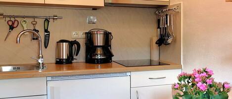 A kitchen with a coffee maker, utensils, and a sink.