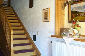 A staircase with wooden steps and blue carpeted handrails, a white radiator, and a framed picture on the wall. - Apartment with 0 bedrooms (Marquartstein)