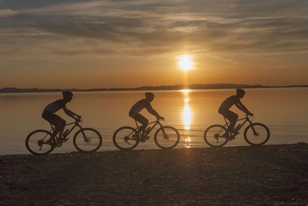 Three cyclists on a beach at sunset.