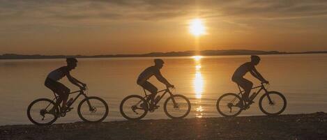 Drei Radfahrer an einem Strand bei Sonnenuntergang.