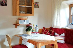 A cozy room with a wooden table, chairs, a red cushioned bench, a cabinet with glass doors, and a window with curtains. - Apartment with 0 bedrooms (Marquartstein)
