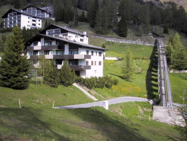 Un immeuble à plusieurs étages, doté de balcons, entouré de verdure et bordé par une voie ferrée.