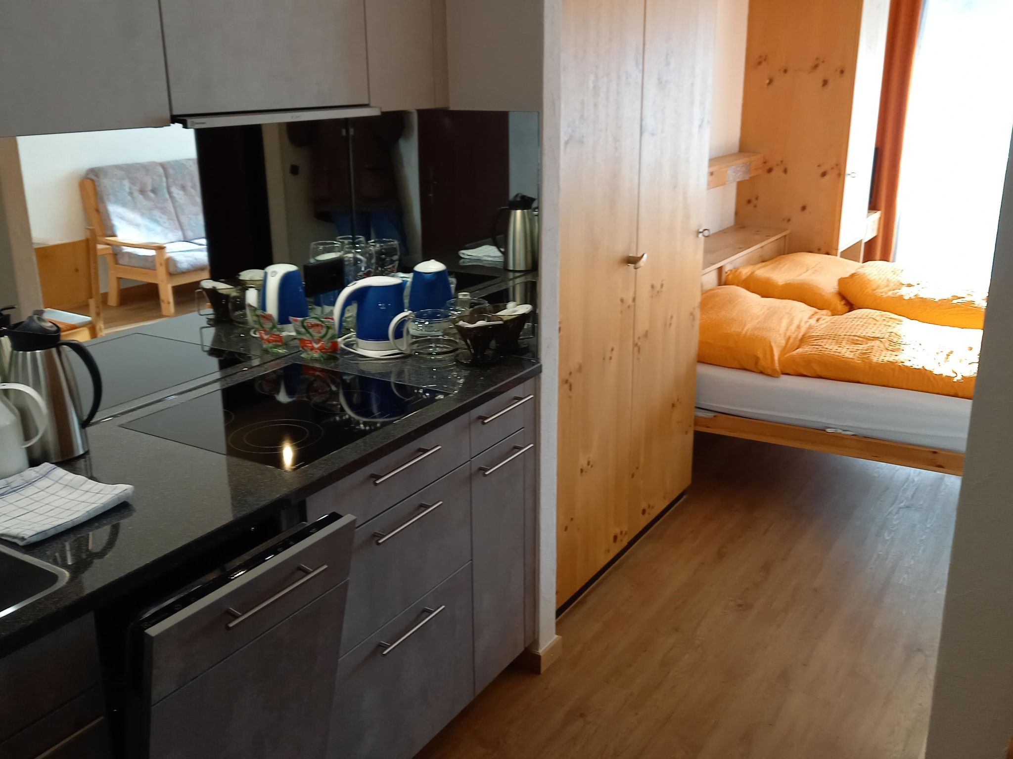 Eine kompakte Küche mit modernen Geräten, ein Essbereich mit einem Stuhl und ein Bett mit orangefarbener Bettwäsche.