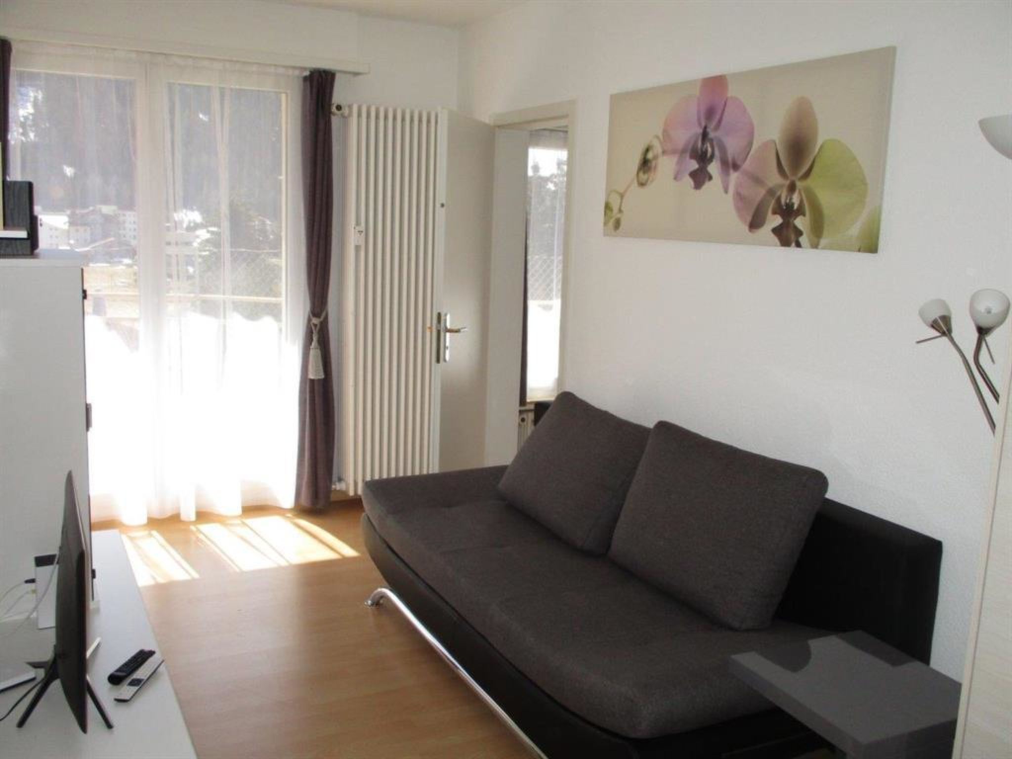 A modern living room with a sofa, a flat-screen TV, and a painting of flowers on the wall.