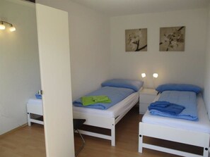 Een kamer met twee eenpersoonsbedden, elk voorzien van een nachtkastje, een lamp en twee aan de muur hangende schilderijen.
