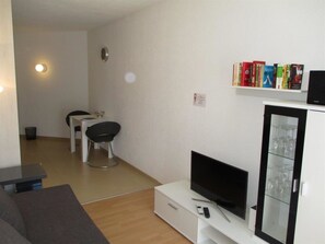 Een woonkamer met een flatscreen televisie, een boekenkast vol boeken, een eethoek met tafel en stoelen, en een glazen kast met glazen.