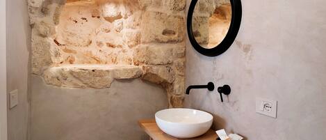 A bathroom with a stone wall, a white sink, and a black faucet.