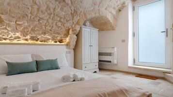 Un dormitorio con pared de piedra, cama con ropa blanca, armario y ventana con vistas.