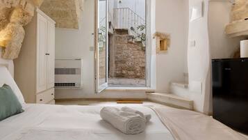 Une chambre avec un lit, une serviette blanche, une armoire, un appareil de climatisation et une vue sur un mur en pierre et un escalier.