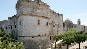 A historic stone castle with battlements, a church with a dome, and a paved walkway with benches.