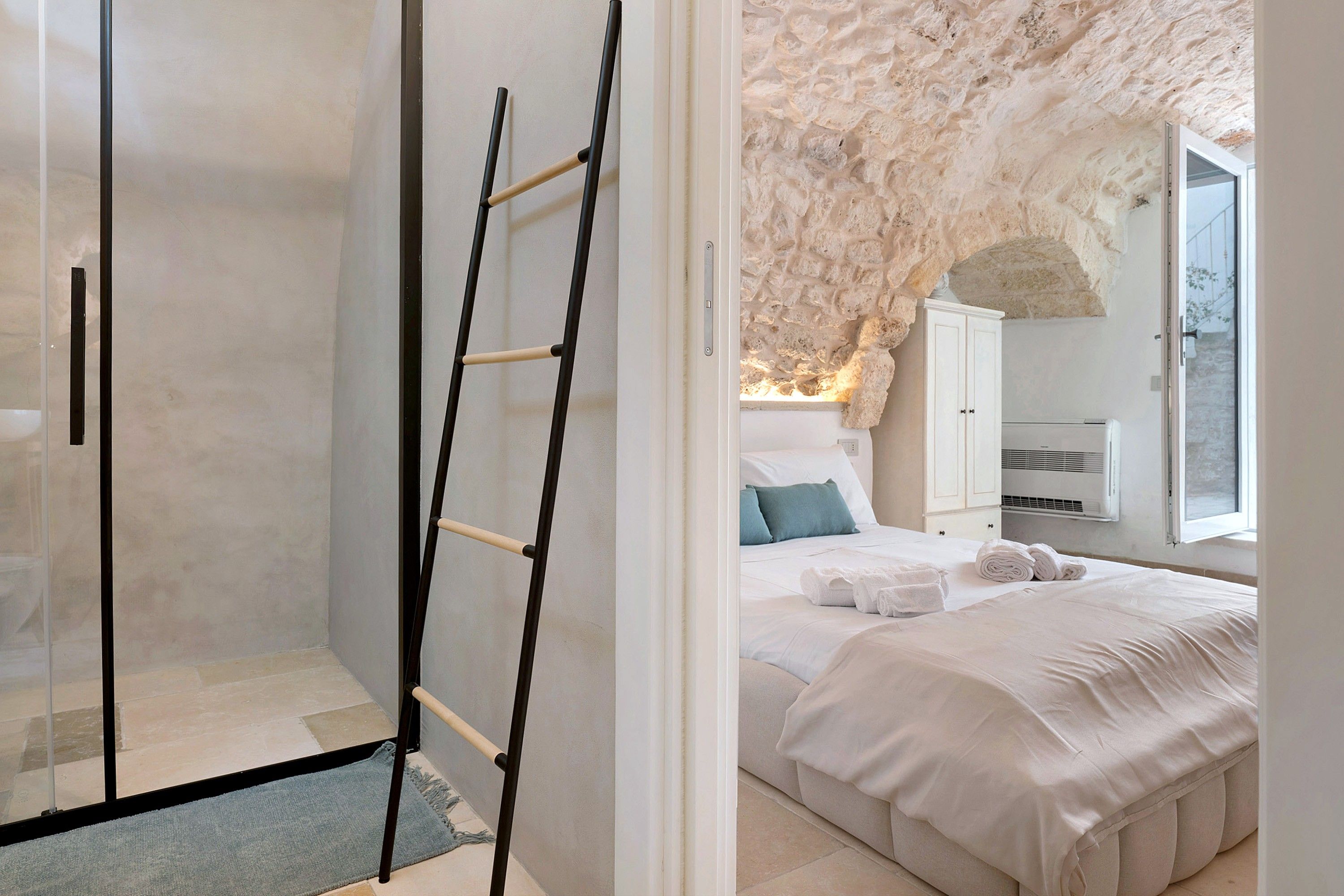 Un dormitorio con una cama, un armario, una escalera y una pared de piedra.