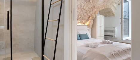 A bedroom with a bed, a wardrobe, a ladder, and a stone wall.