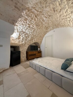A bedroom with a stone ceiling, a bed, a TV, and a wooden dresser. - Terra Mia Double Suite Room with Wi-Fi and Air Conditioning (Carovigno)