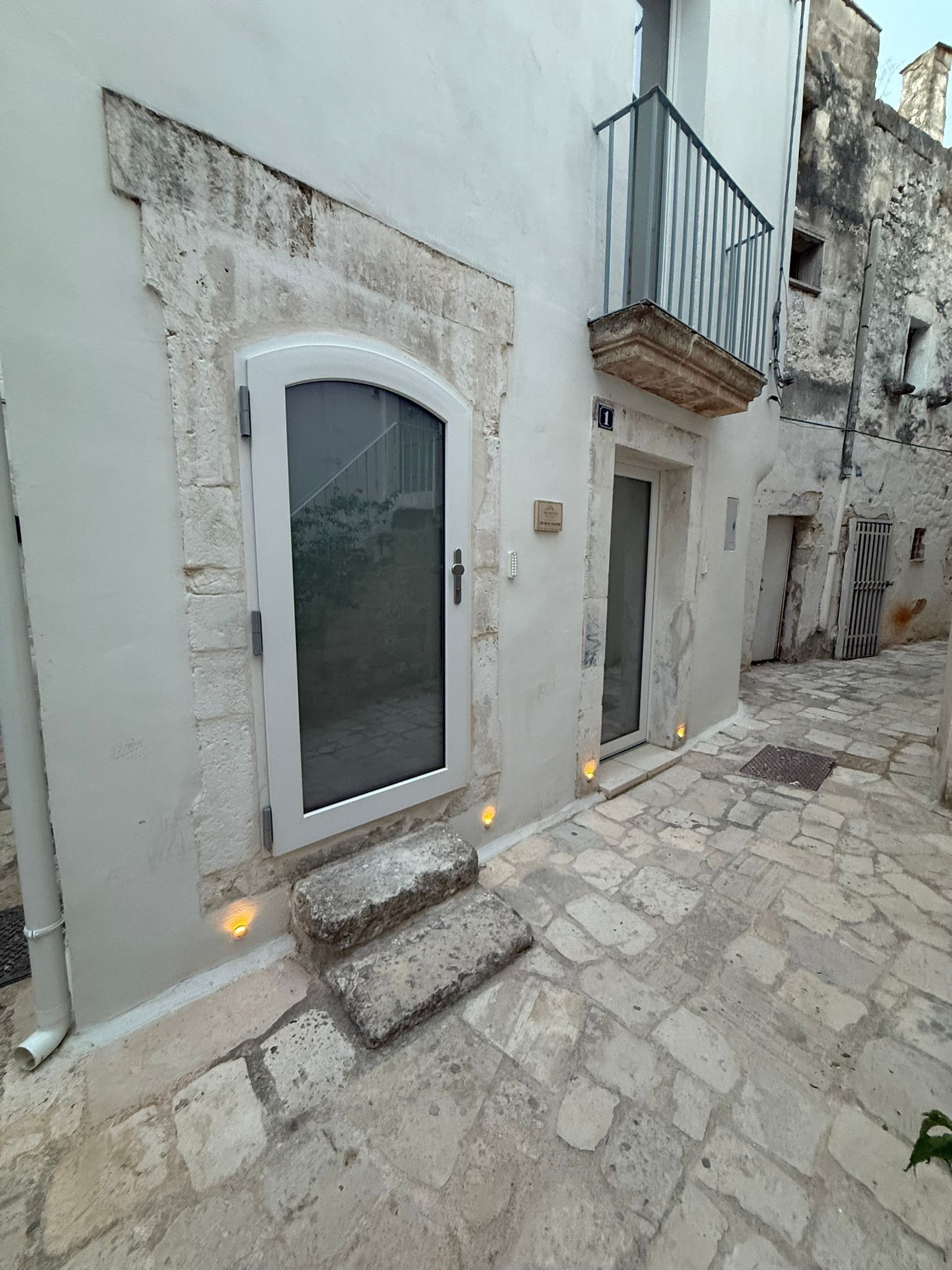Un bâtiment doté d’une grande porte en arc de cercle, d’un petit balcon et d’une cour pavée de pierres.