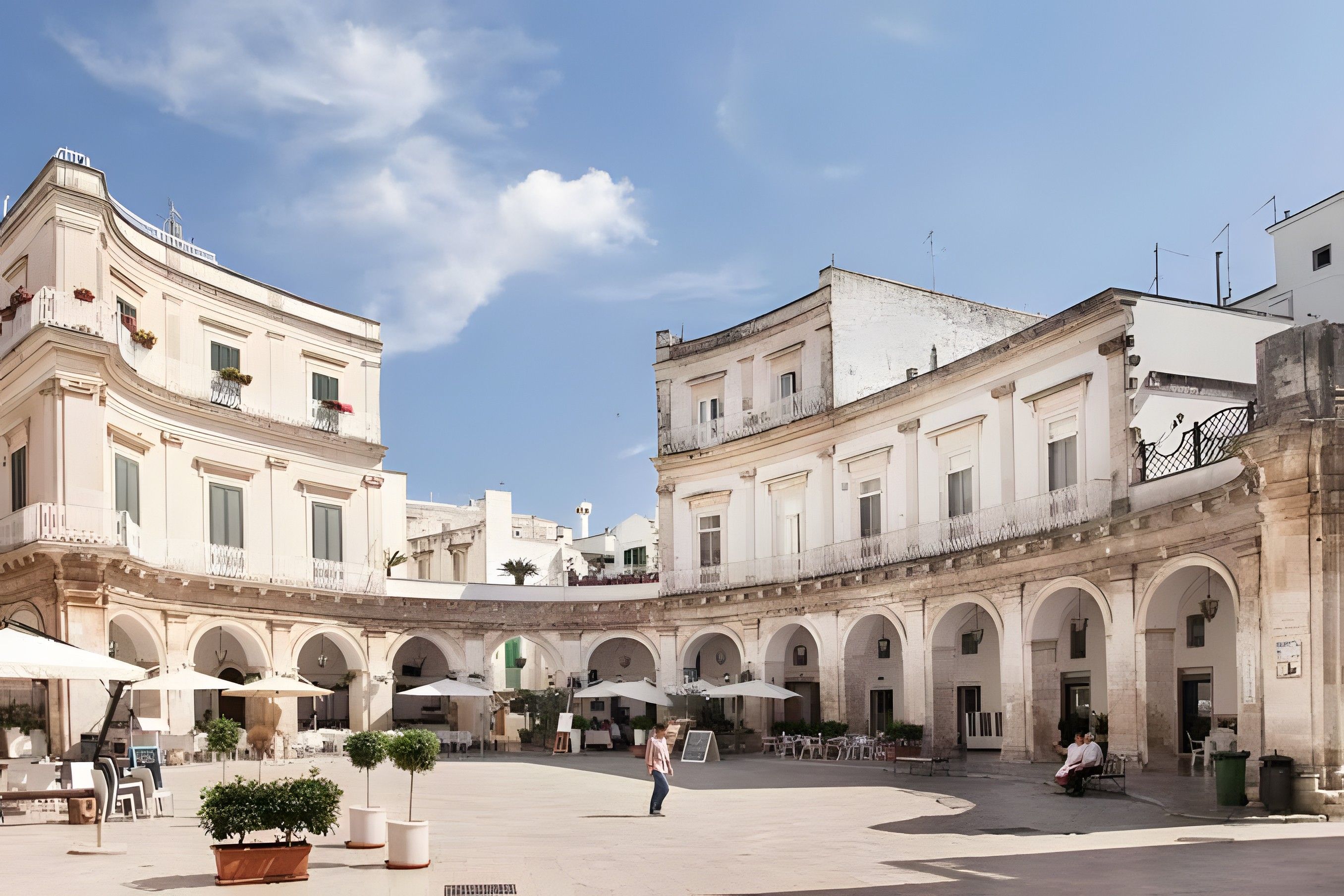 A spacious courtyard with a central open area surrounded by buildings with classical architecture, featuring arches and columns.