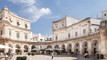 A spacious courtyard with a central open area surrounded by buildings with classical architecture, featuring arches and columns.