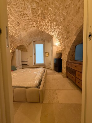 An attic bedroom with a stone ceiling, a bed, a dresser, and a refrigerator. - Terra Mia Double Suite Room with Wi-Fi and Air Conditioning (Carovigno)